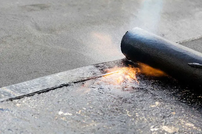 Close-up of a torch-on felt roof being heat-sealed along a lap joint